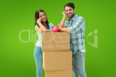 Composite image of happy young couple with moving boxes and pigg