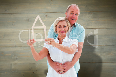 Composite image of happy older couple holding house shape