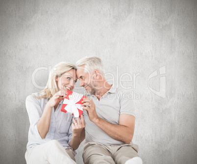 Composite image of happy couple sitting and holding present