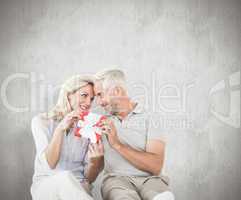 Composite image of happy couple sitting and holding present