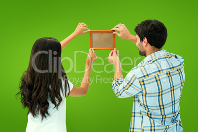 Composite image of happy young couple putting up picture frame