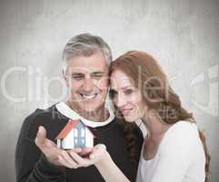Composite image of casual couple holding small house