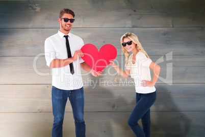 Composite image of cool young couple holding red heart