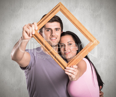Composite image of young couple holding up frame