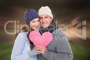 Composite image of happy couple in warm clothing holding heart