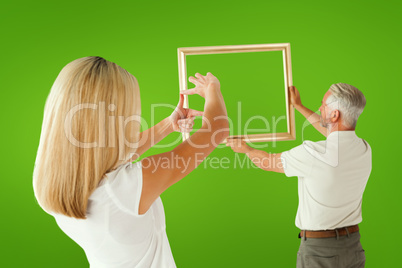 Composite image of couple hanging a frame together