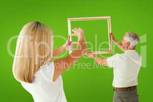 Composite image of couple hanging a frame together