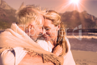 Smiling couple sitting on the beach under blanket