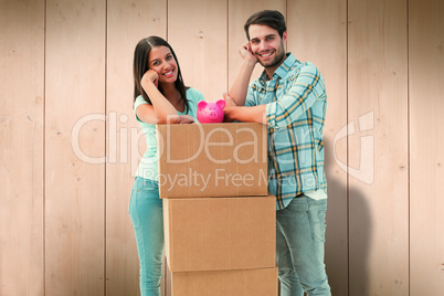 Composite image of happy young couple with moving boxes and pigg