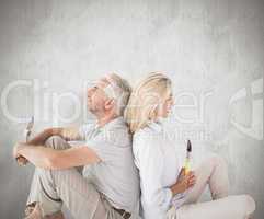 Composite image of happy couple sitting and holding paintbrushes