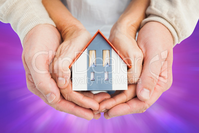 Composite image of couple holding small model house in hands