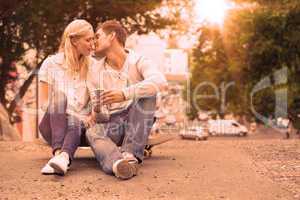 Cute young couple sitting on skateboard kissing