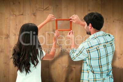 Composite image of happy young couple putting up picture frame