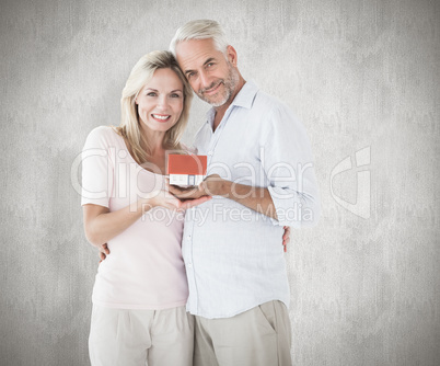 Composite image of happy couple holding miniature model house