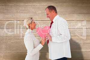 Composite image of older affectionate couple holding pink heart