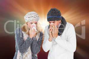 Composite image of sick couple in winter fashion sneezing