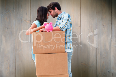 Composite image of happy young couple with moving boxes and pigg