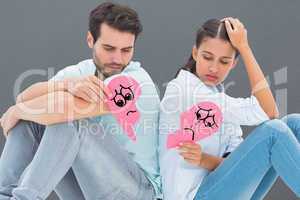 Composite image of sad couple sitting holding two halves of brok