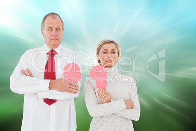 Composite image of older couple standing holding broken pink hea