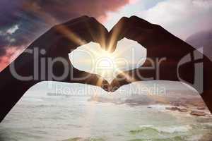Composite image of hands making heart shape on the beach