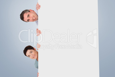 Composite image of woman and man hiding behind a blank panel