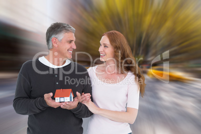 Composite image of casual couple holding small house