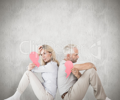 Composite image of unhappy couple sitting holding two halves of