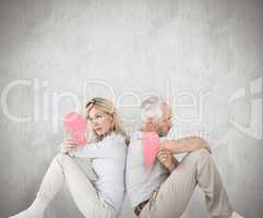 Composite image of unhappy couple sitting holding two halves of