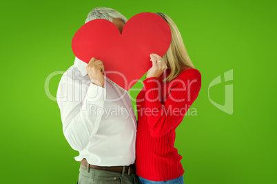 Composite image of couple embracing and holding heart over faces