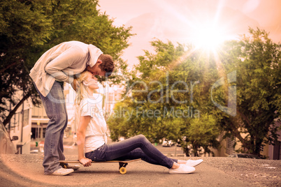 Hip young blonde sitting on skateboard with boyfriend kissing fo
