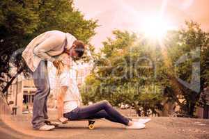 Hip young blonde sitting on skateboard with boyfriend kissing fo