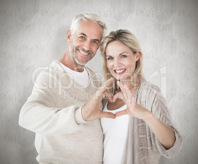 Composite image of happy couple forming heart shape with hands