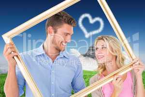 Composite image of attractive young couple holding picture frame