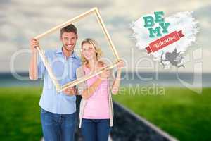 Composite image of attractive young couple holding picture frame