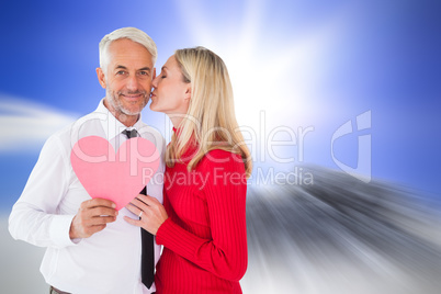 Composite image of handsome man holding paper heart getting a ki