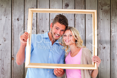 Composite image of attractive young couple holding picture frame