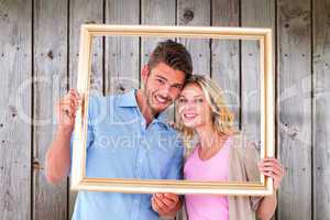 Composite image of attractive young couple holding picture frame