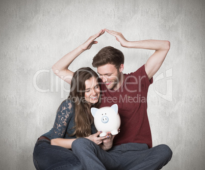 Composite image of couple sitting on floor with piggy bank Composite image of couple sitting on floor with piggy bank
