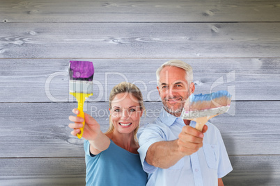 Composite image of happy couple holding paintbrushes smiling at