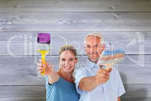 Composite image of happy couple holding paintbrushes smiling at