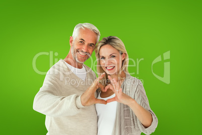 Composite image of happy couple forming heart shape with hands