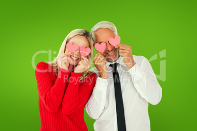 Composite image of silly couple holding hearts over their eyes