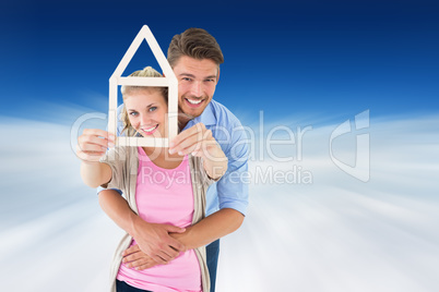 Composite image of young couple hugging and holding house outlin Composite image of young couple hugging and holding house outlin