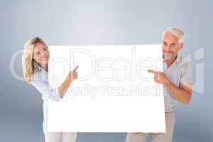 Composite image of happy couple holding and pointing to large po