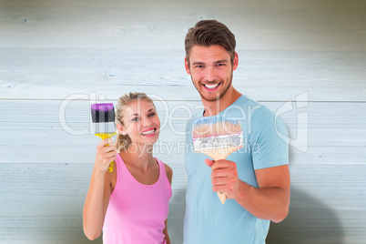 Composite image of young couple smiling and holding paintbrushes