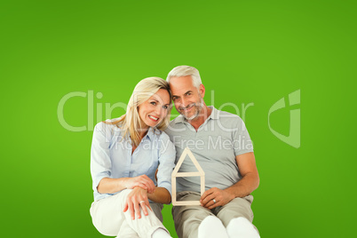 Composite image of happy couple sitting and holding house outlin