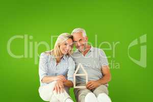 Composite image of happy couple sitting and holding house outlin