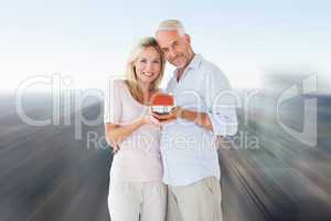 Composite image of happy couple holding miniature model house