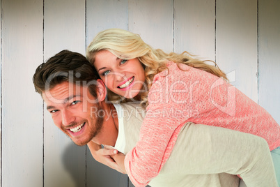 Composite image of handsome man giving piggy back to his girlfri