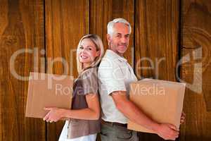 Composite image of happy couple holding moving boxes